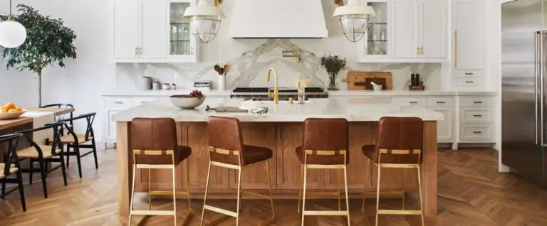 Kitchen with white cabinets, marble backsplash, brass fixtures, and a walnut island with leather bar stools